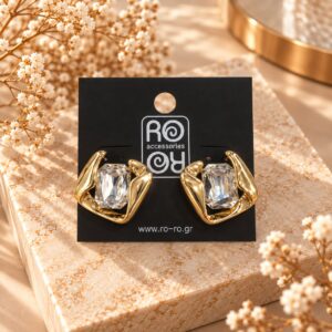 RO Accessories Crystal Sculpture χρυσά σκουλαρίκια με μεγάλη διάφανη ορθογώνια πέτρα και ασύμμετρες μεταλλικές καμπύλες.